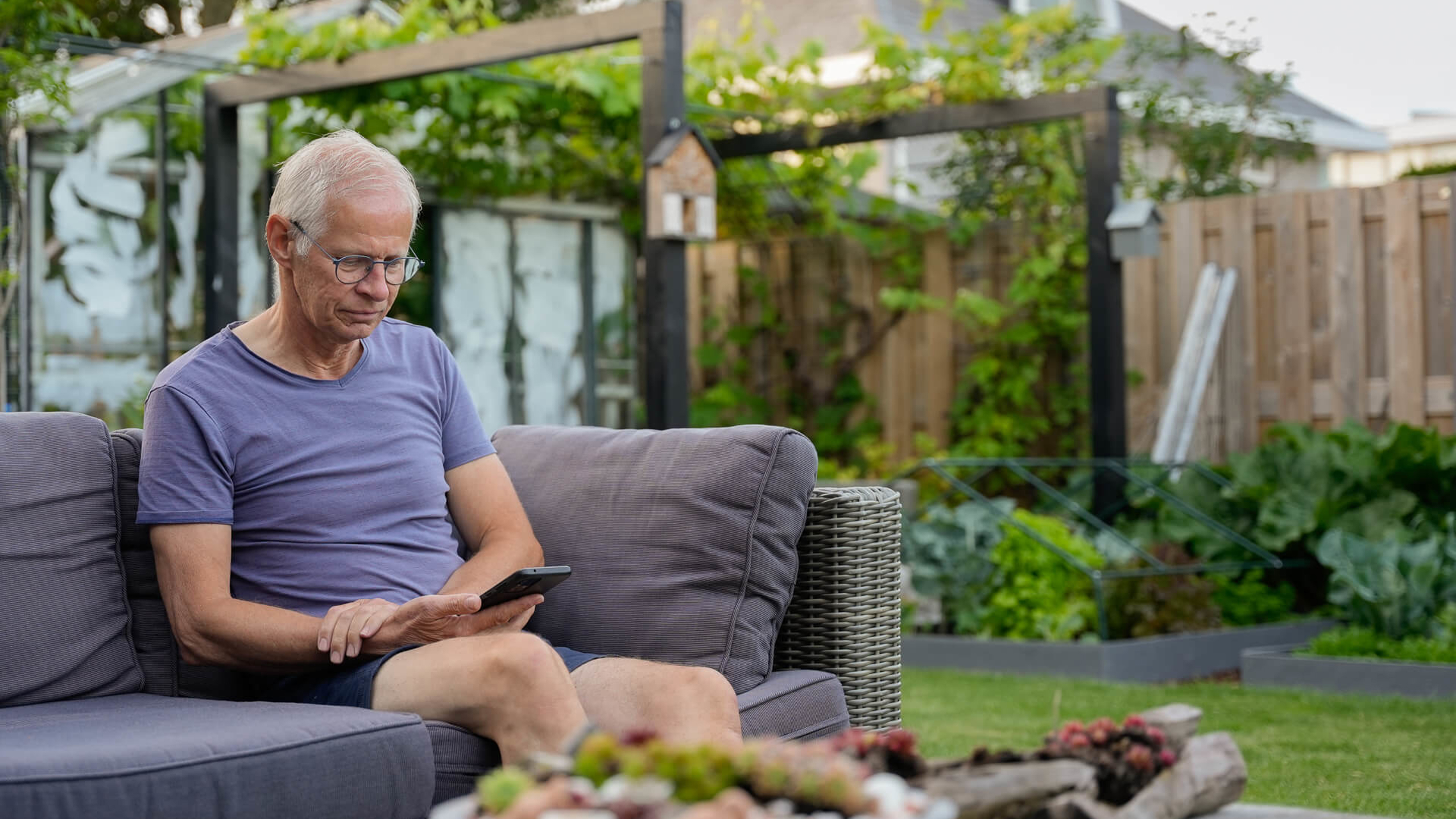 Man kijkt in zijn tuin op zijn telefoon naar de HR Energy app, waarmee hij de prestaties van zijn PVT-systeem kan bekijken.