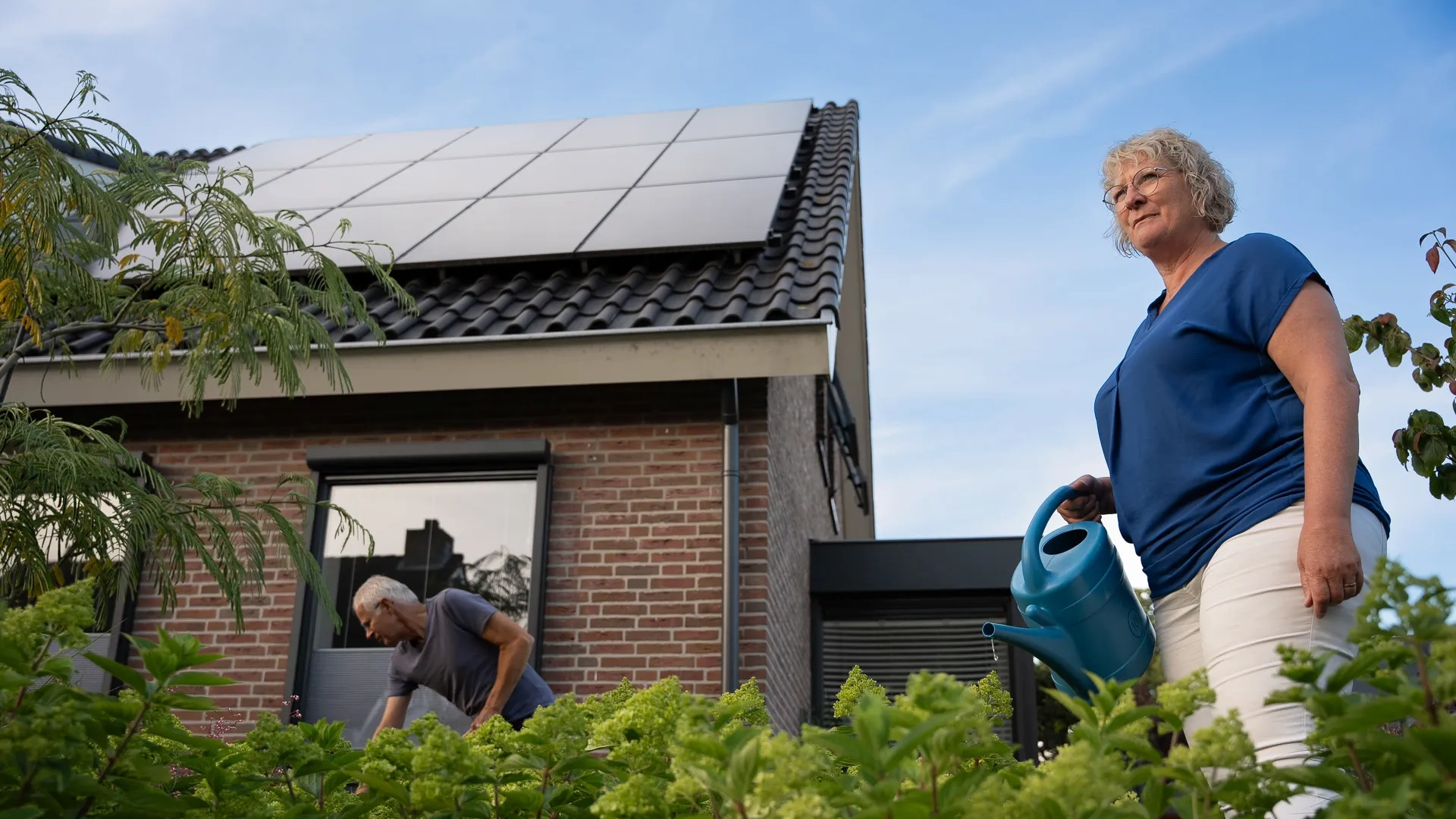 Man en vrouw bezig in voorruin achter hen staat hun huis met PVT-panelen op het dak