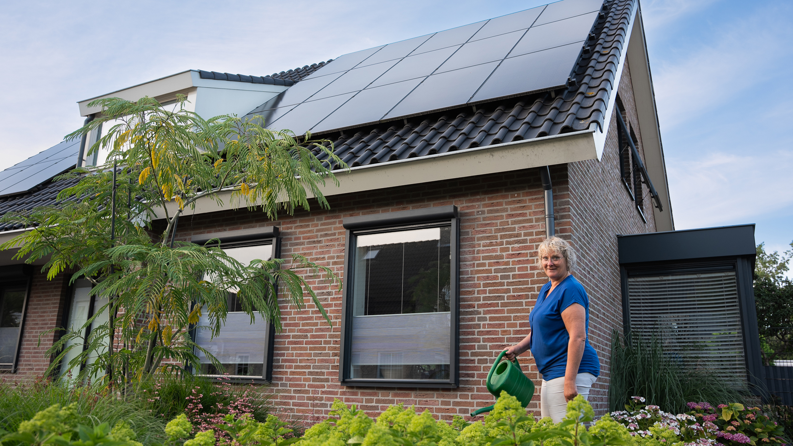 Vrouw in haar tuin met PVT panelen op het dak, onderdeel van het PVT systeem van HR energy
